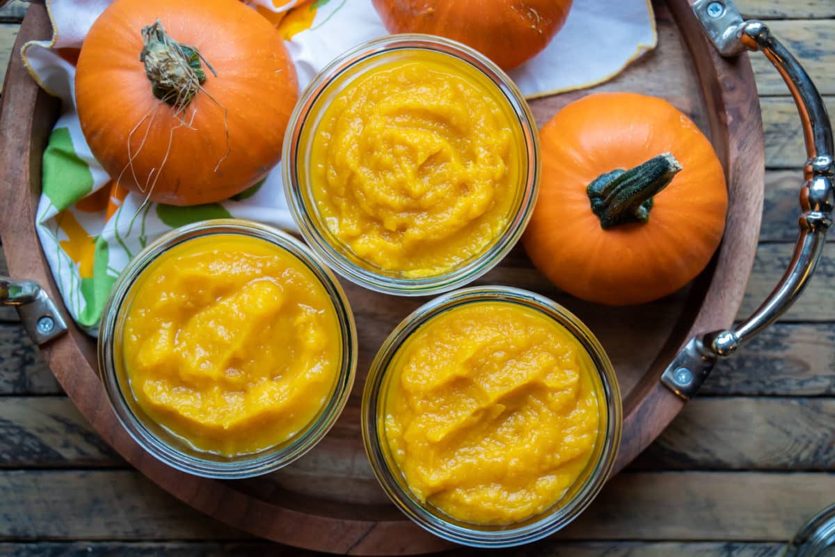 3 glass jars of pumpkin puree. 2 mini pumpkins next to them.