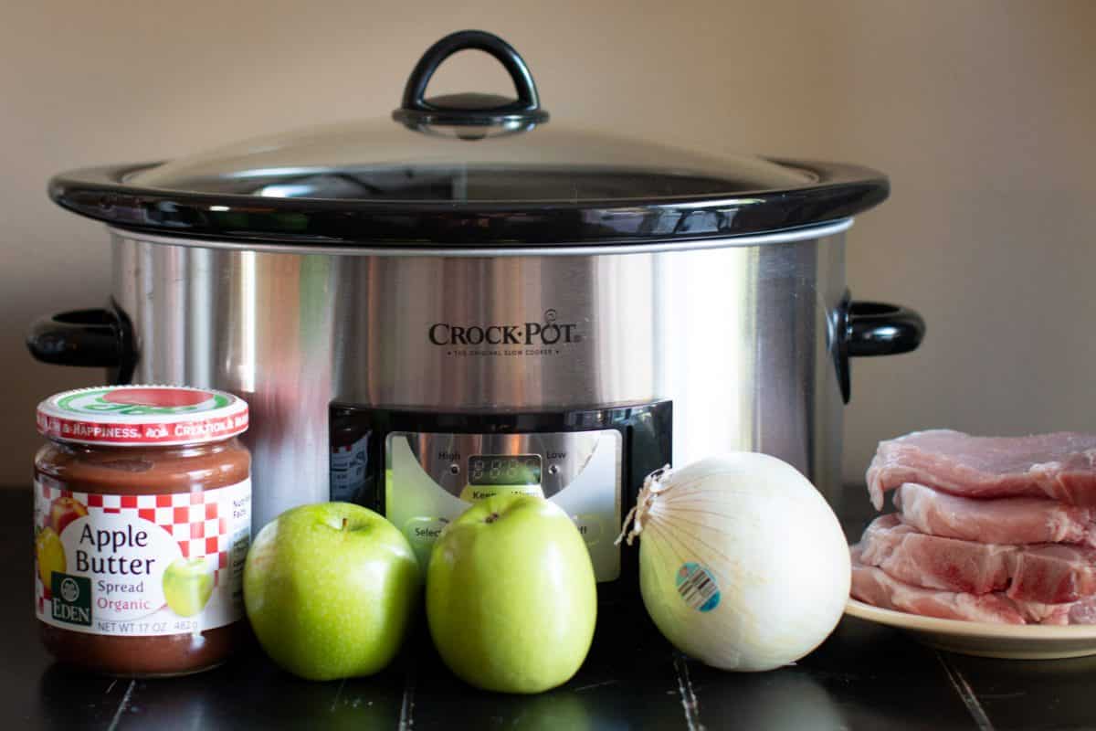 pork chops, apple butter, apples, white onion in front of a slow cooker.