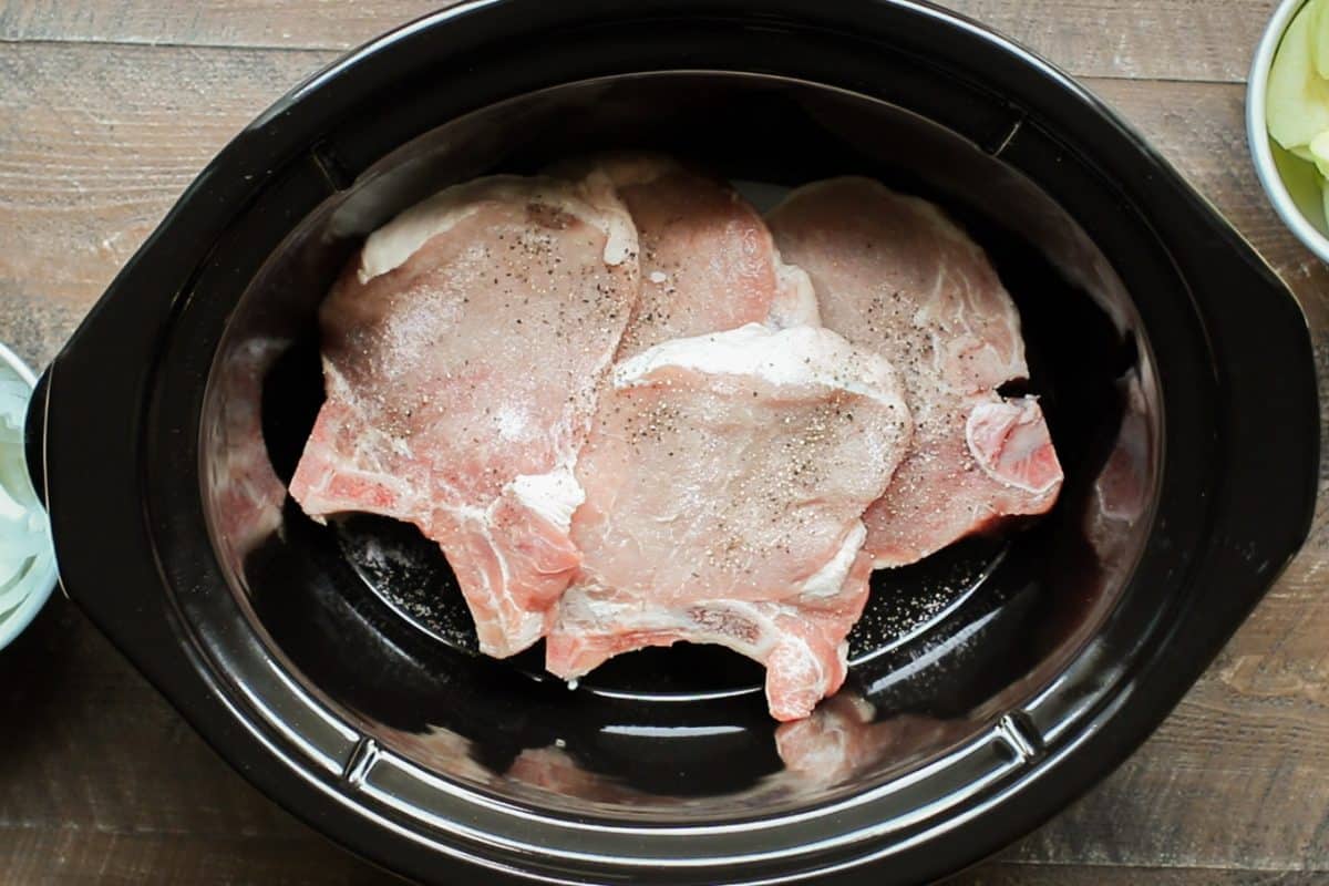 4 large pork chops in an oval black slow cooker.