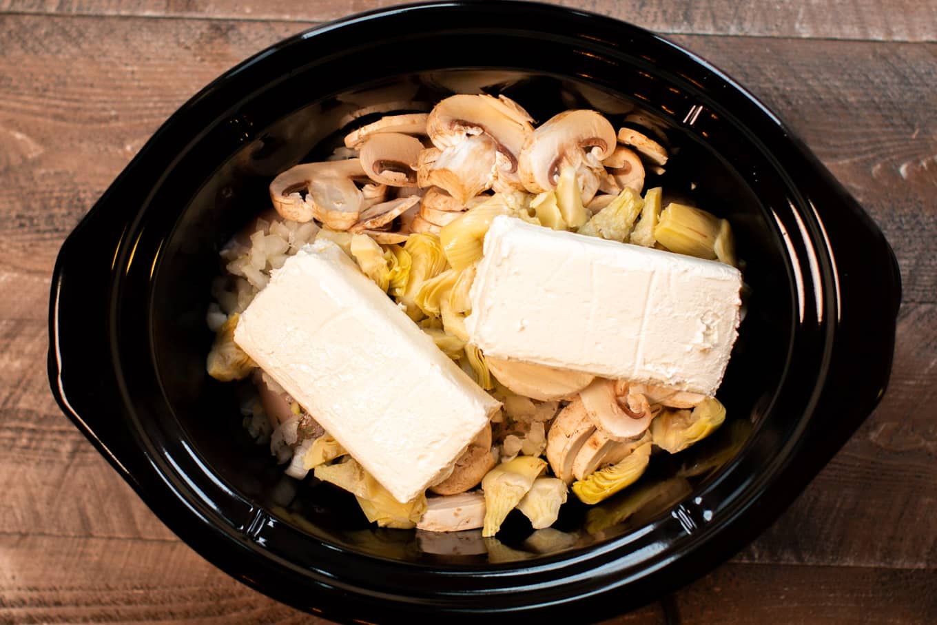 artichoke mushroom chicken in slow cooker with cream cheese blocks on top