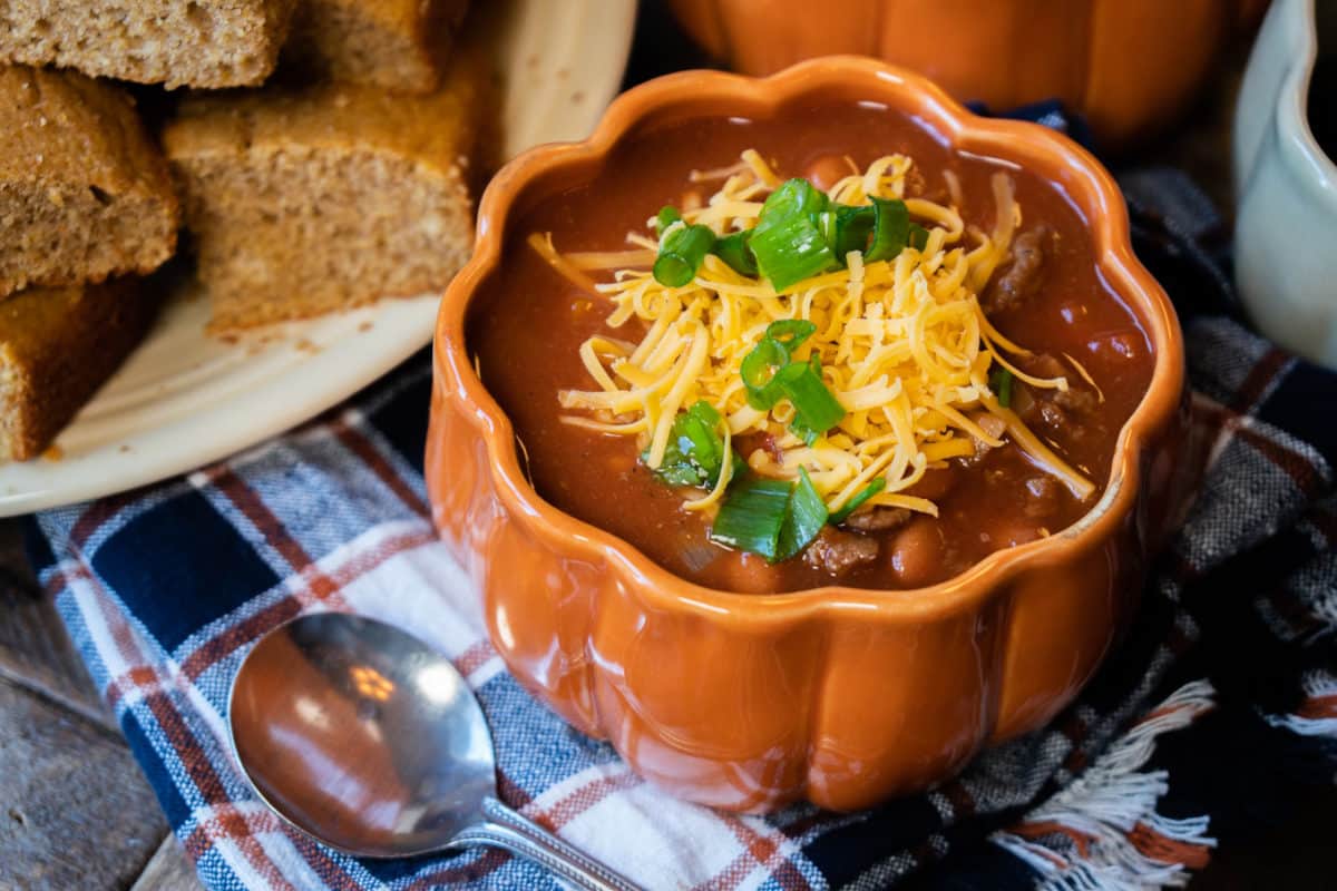 pumpkin shaped bowl with pumpkin chili in it. Cheese and green onion on top.