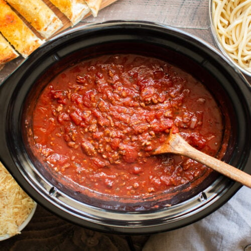 cooked spaghetti in a slow cooker with garlic bread and noodles on the side.