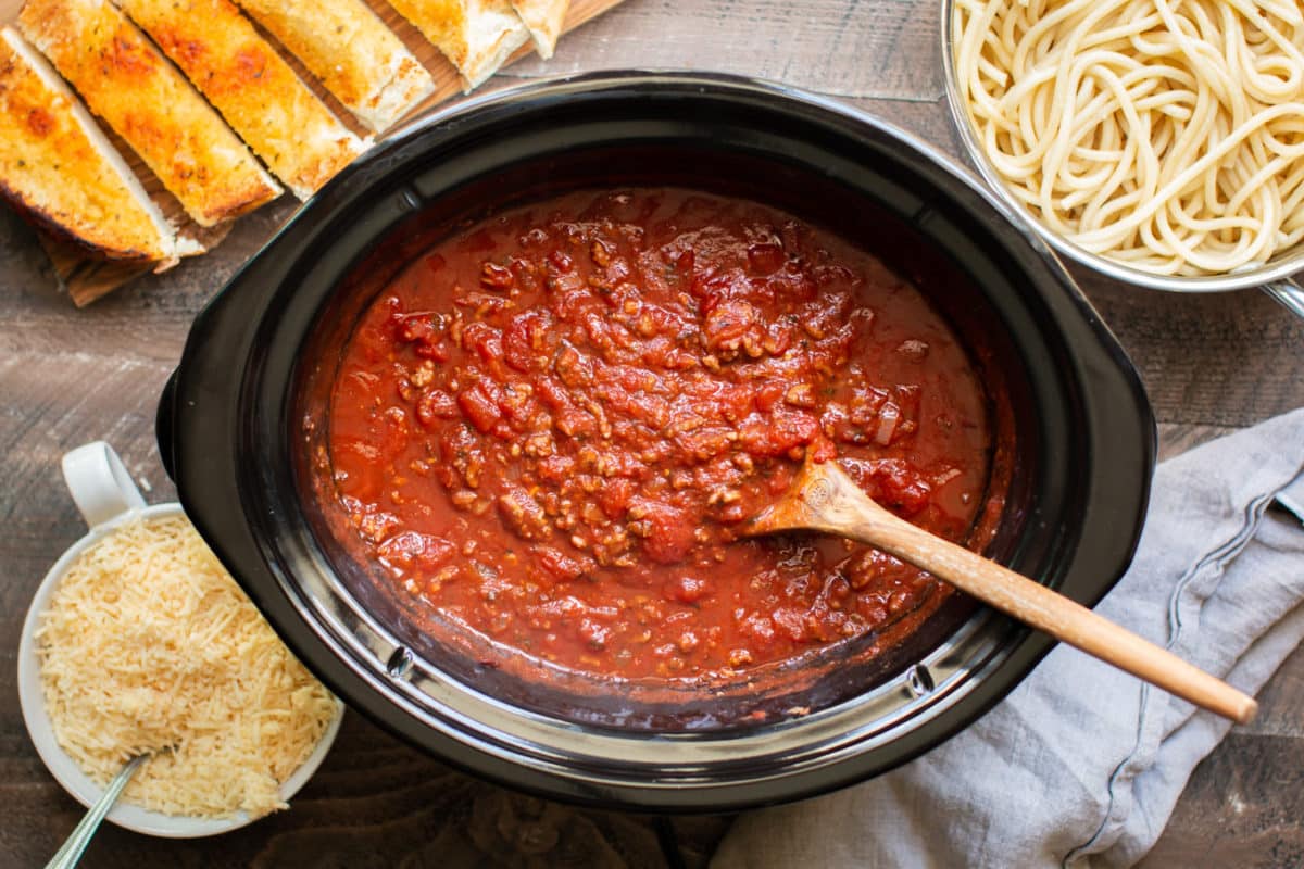 cooked spaghetti in a slow cooker with garlic bread and noodles on the side.