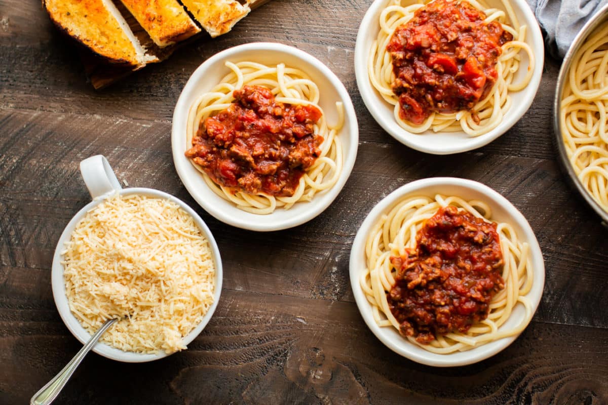 3 bowls of spaghetti with sauce on top.