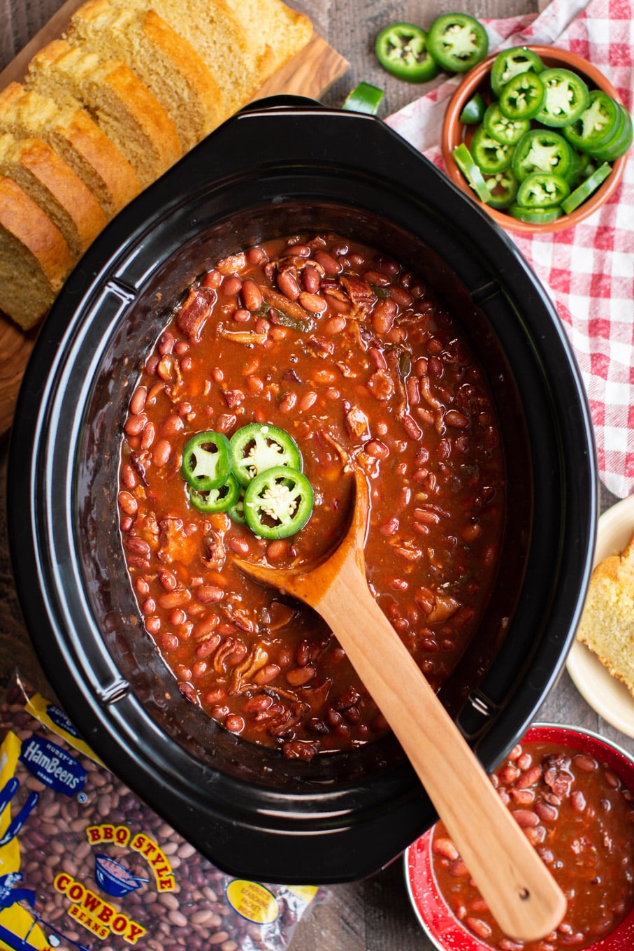 spicy barbecue beans cooked in the slow cooker with wooden spoon in them.
