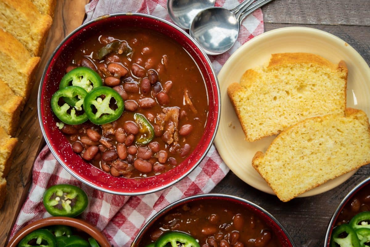 two red bowls of bbq beans with cornbread on the side.