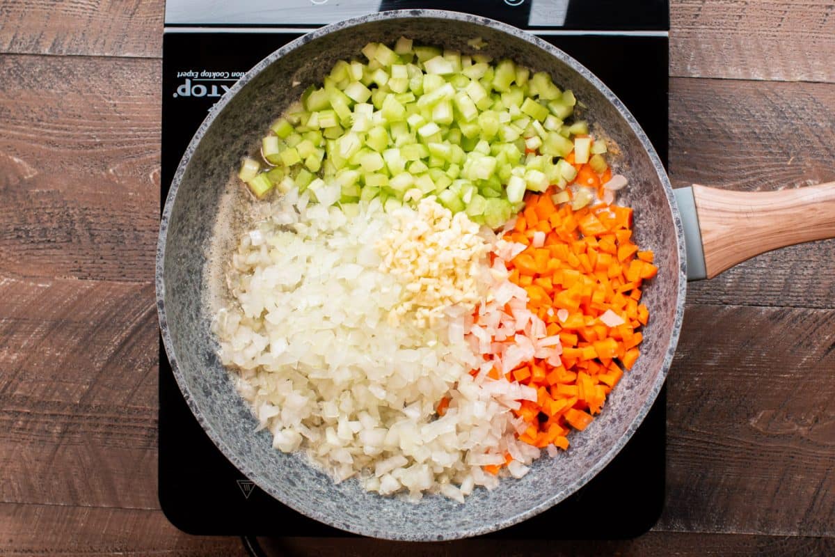 onion, celery, garlic and onion in a frying pan on a burner.