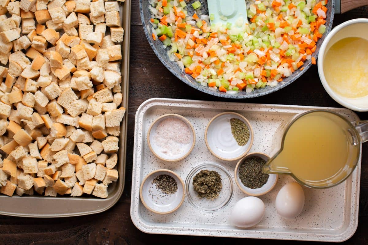 bread cubes on a sheet pan. Vegetables in skillet. Seasonings, chicken broth and eggs on small tray.