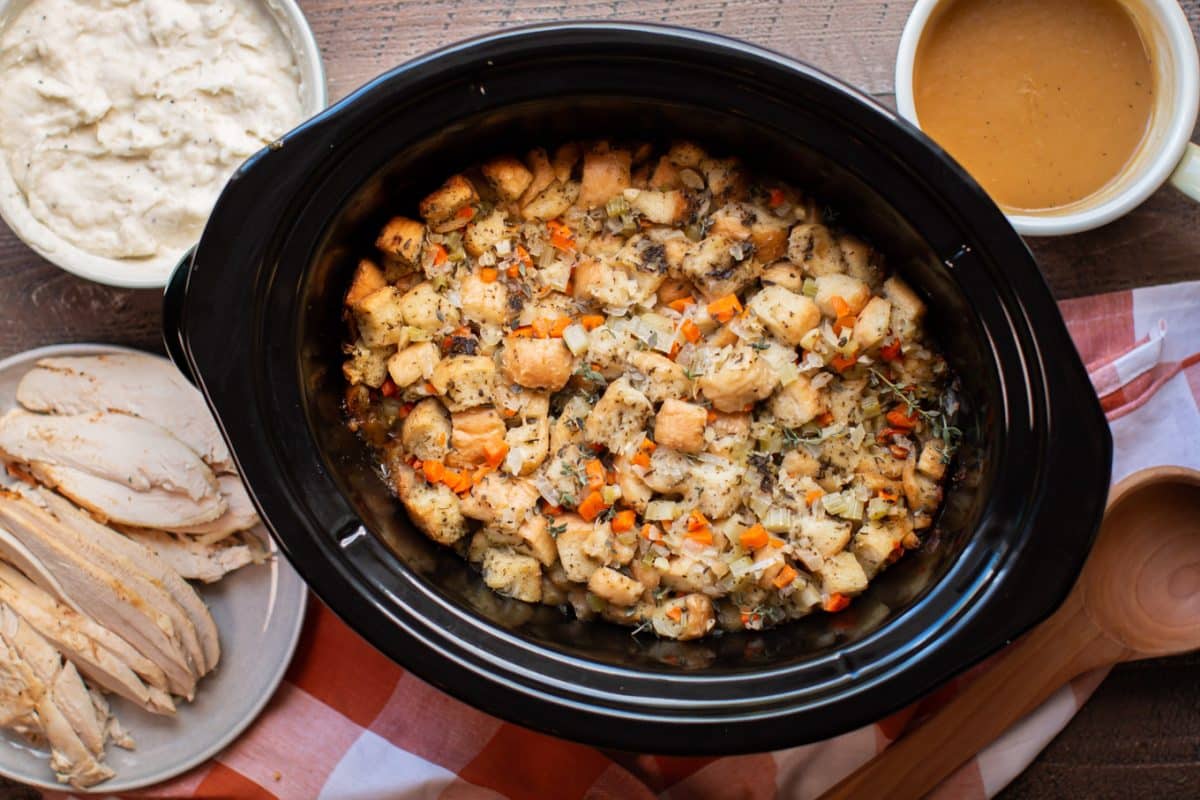 bread stuffing in a slow cooker with turkey, gravy and mashed potatoes on the side.