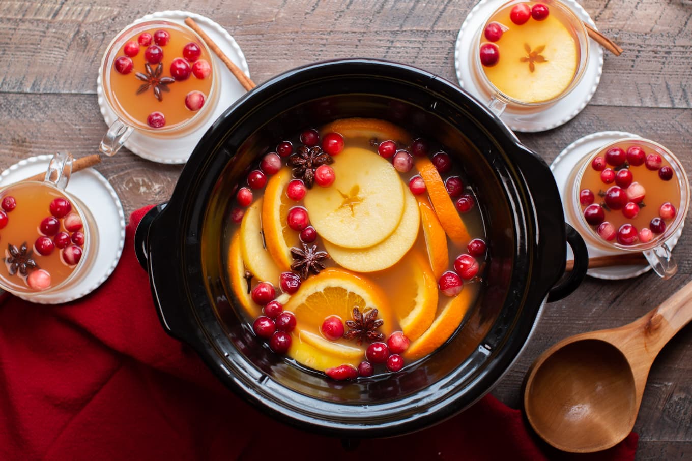 Finished apple cider in slow cooker with cider in mugs around the sides.