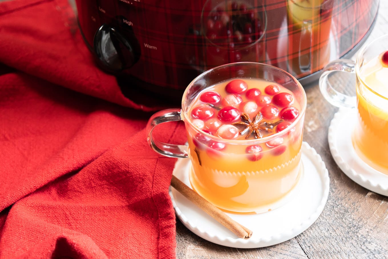 Clear mug of apple cider with plaid slow cooker in the background.