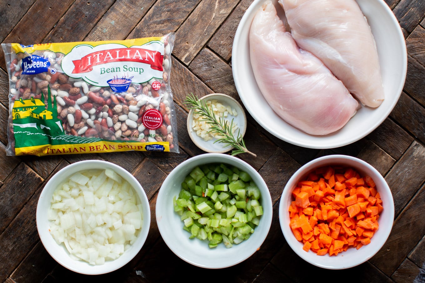 Bag of beans. Turkey breasts, onion, carrots, celery, garlic, rosemary in dished on wood table.