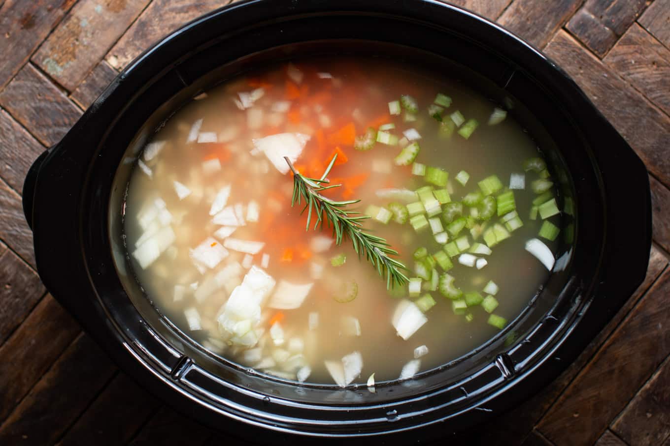 Uncooked soup in the slow cooker. Rosemary spring on top.