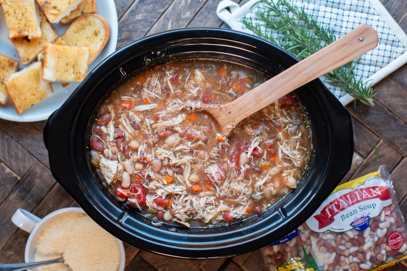 wooden spoon serving Cooked Italian bean soup, garlic bread on the side.