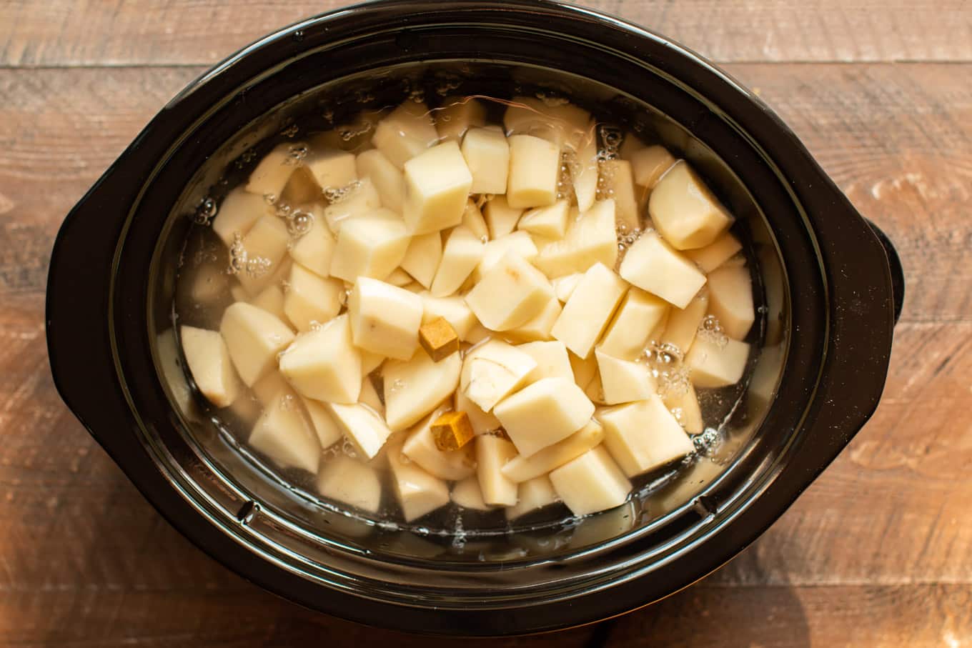 raw potatoes in water with chicken bouillon cubes on top.