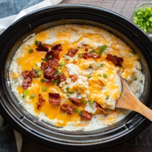 slow cooker full of baked potato casserole with wooden spoon in it.