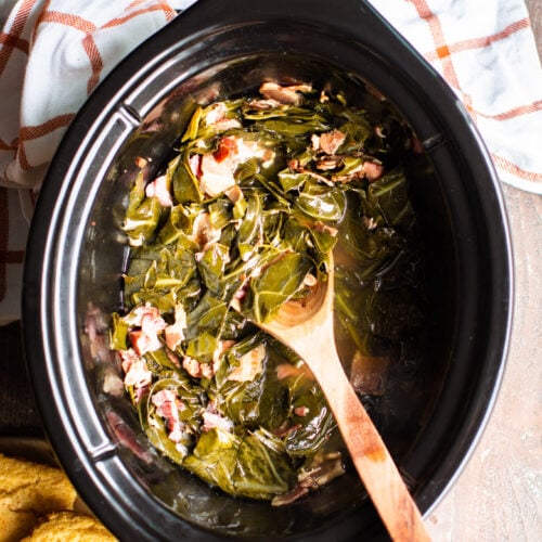 collard greens in the slow cooker with wooden serving spoon in them.