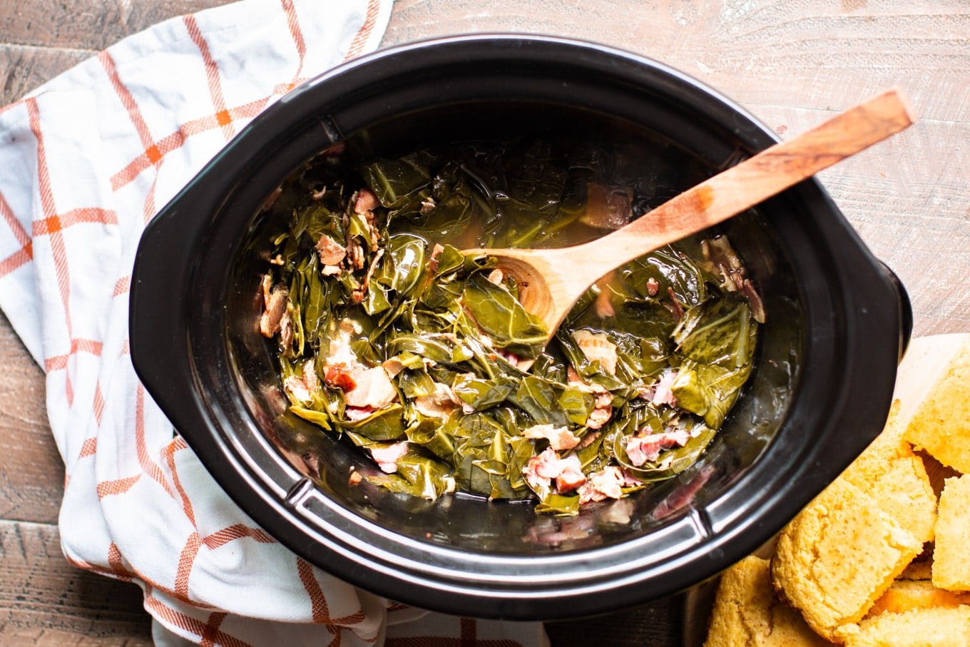 Finished collard green in slow cooker with spoon and cornbread