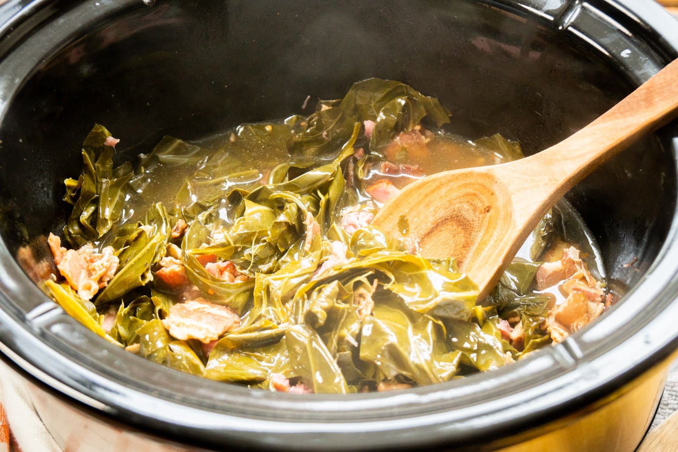 cooked collard greens in slow cooker with broth and spoon