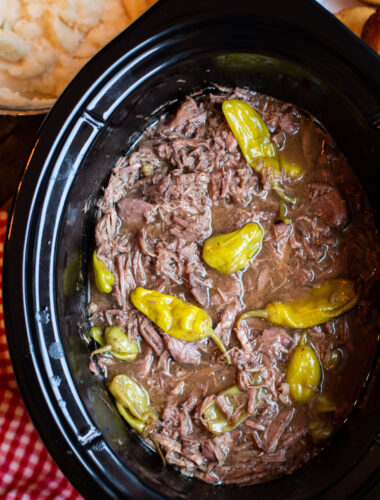 close up of pot roast with pepperoncinis in sauce in slow cooker.