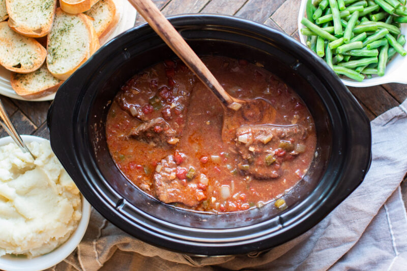 finished swiss steak in slow cooker with wooden serving spatula