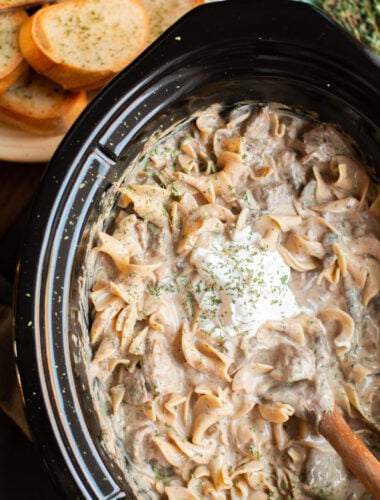 close up of stroganoff in slow cooker with dollop of sour cream.
