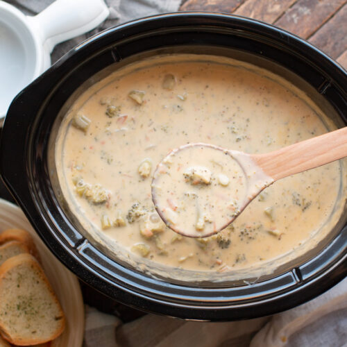 broccoli cheese soup with large wooden spoon scooping soup out