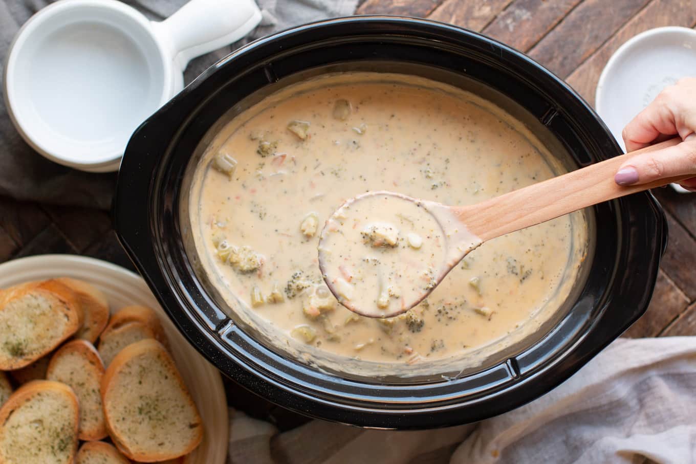 broccoli cheese soup with large wooden spoon scooping soup out