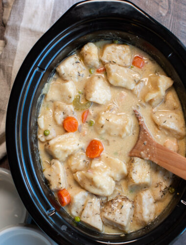 chicken and dumplings cooked in slow cooker with wooden spoon in it.