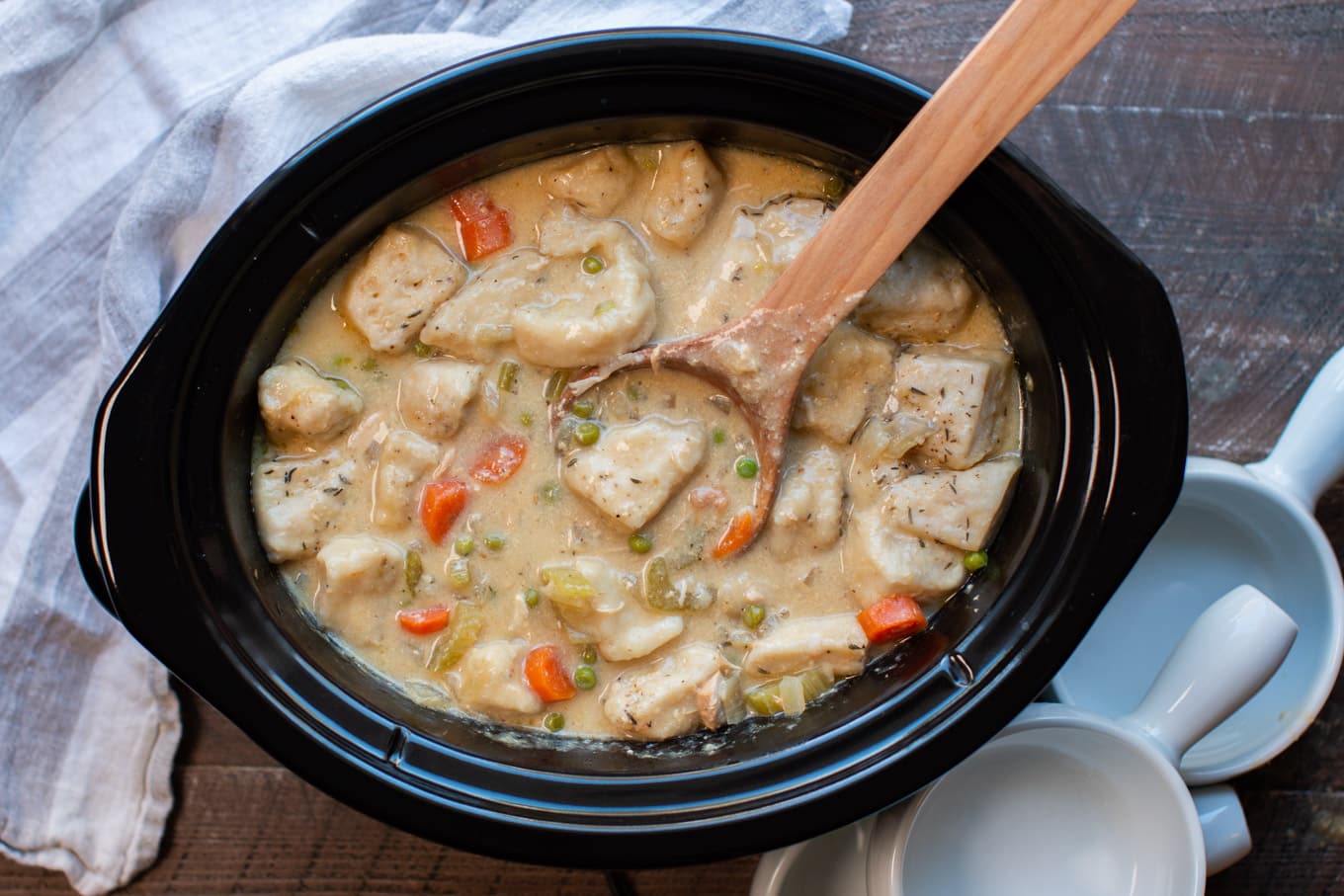 serving chicken and dumplings in slow cooker with wooden spoon.