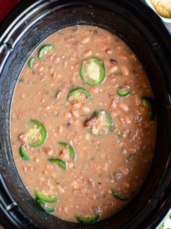 spicy pinto beans in a slow cooker with jalapenos on top.