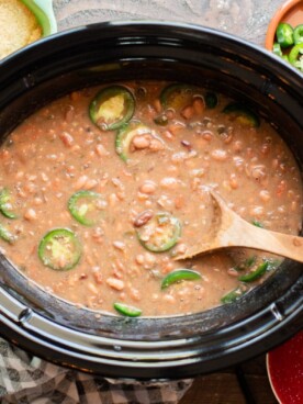 pinto beans in the slow cooker cooked with wooden spoon in them.