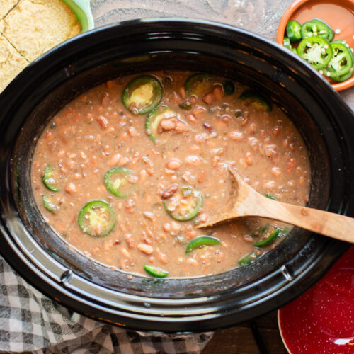 pinto beans in the slow cooker cooked with wooden spoon in them.