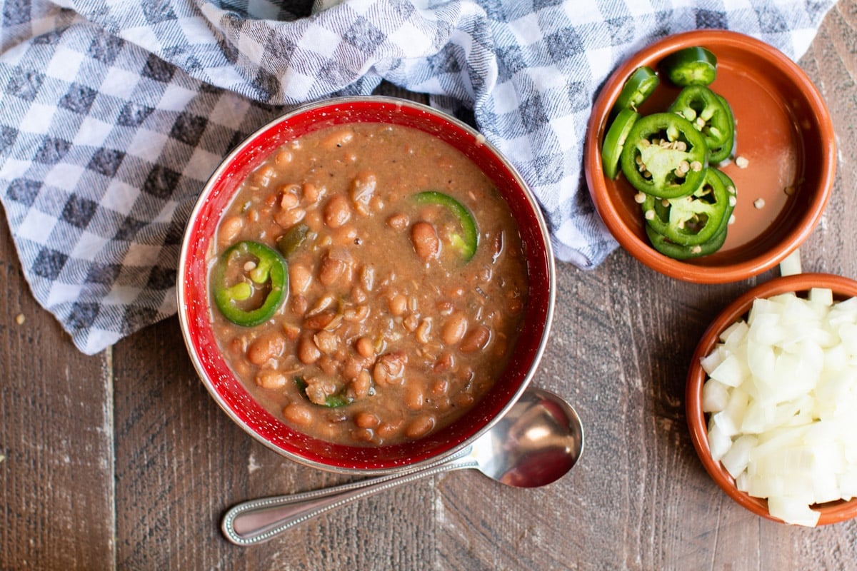 red bowl with pinto beans in it. Jalapenos and onions on side.