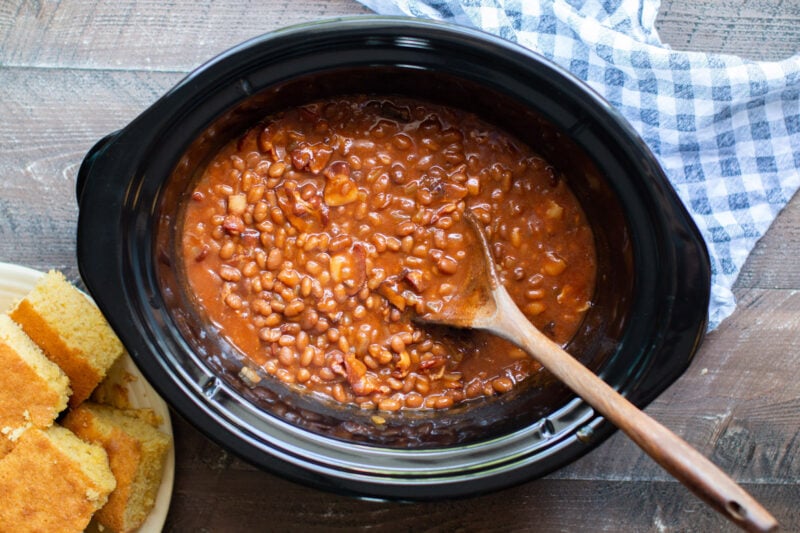 baked beans cooked in the slow cooker with wooden spoon in them.