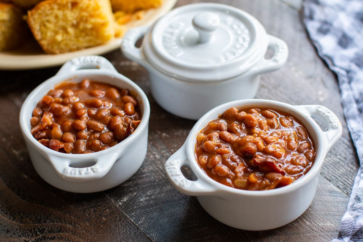 baked beans in small white bowls with cornbread in background.