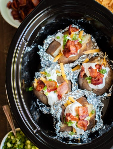 close up of baked potatoes in foil, halfway unwrapped with toppings