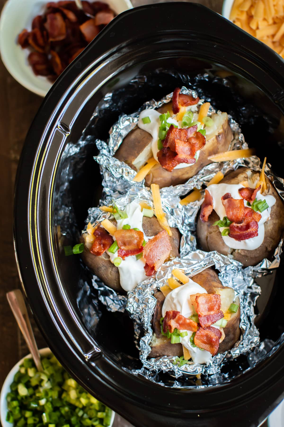close up of baked potatoes in foil, halfway unwrapped with toppings