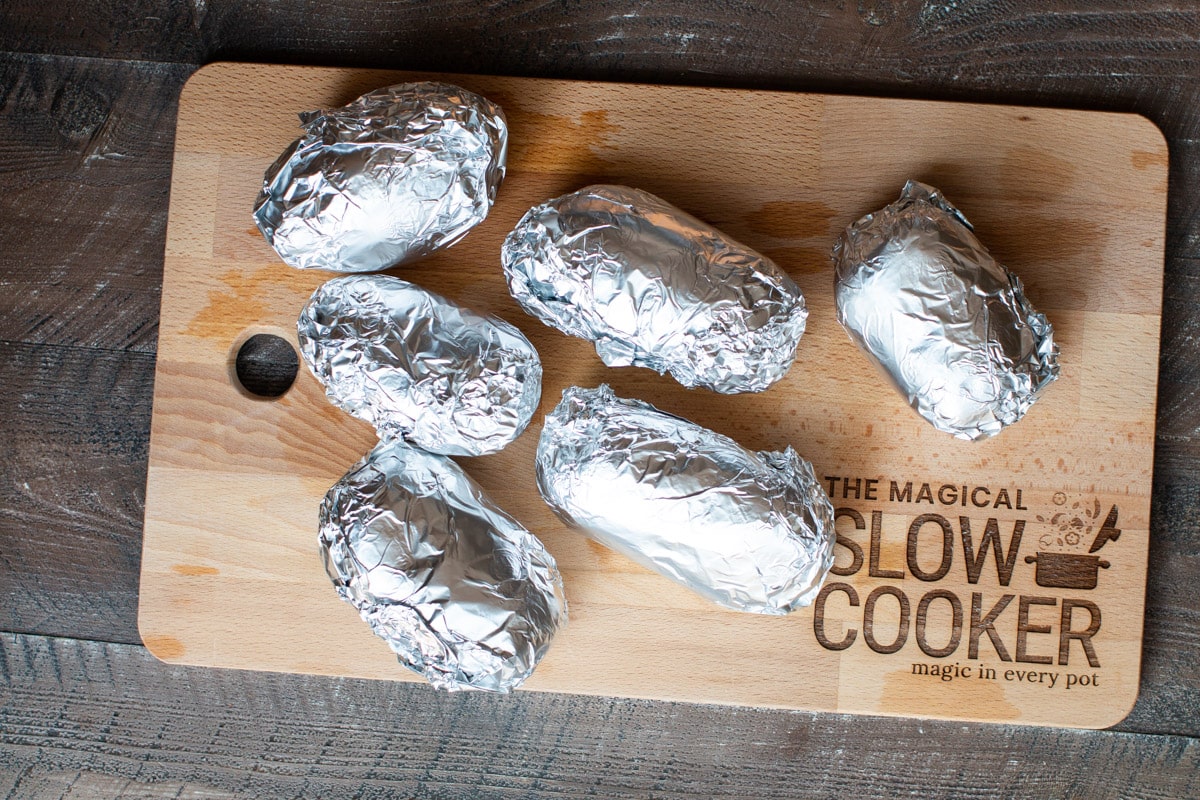 6 potatoes wrapped in foil on cutting board