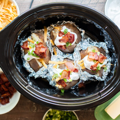 baked potatoes in slow cooker halfway wrapped in foil with toppings.