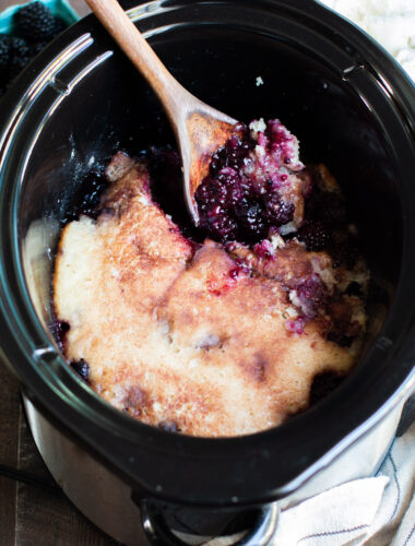 blackberry cobbler in slow cooker with spoon in it. Ice cream in the background