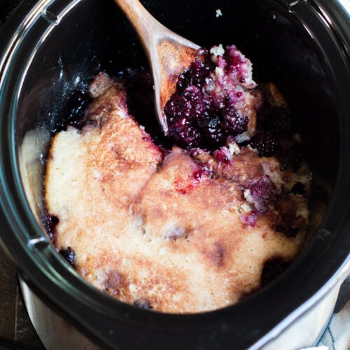 blackberry cobbler in slow cooker with spoon in it. Ice cream in the background