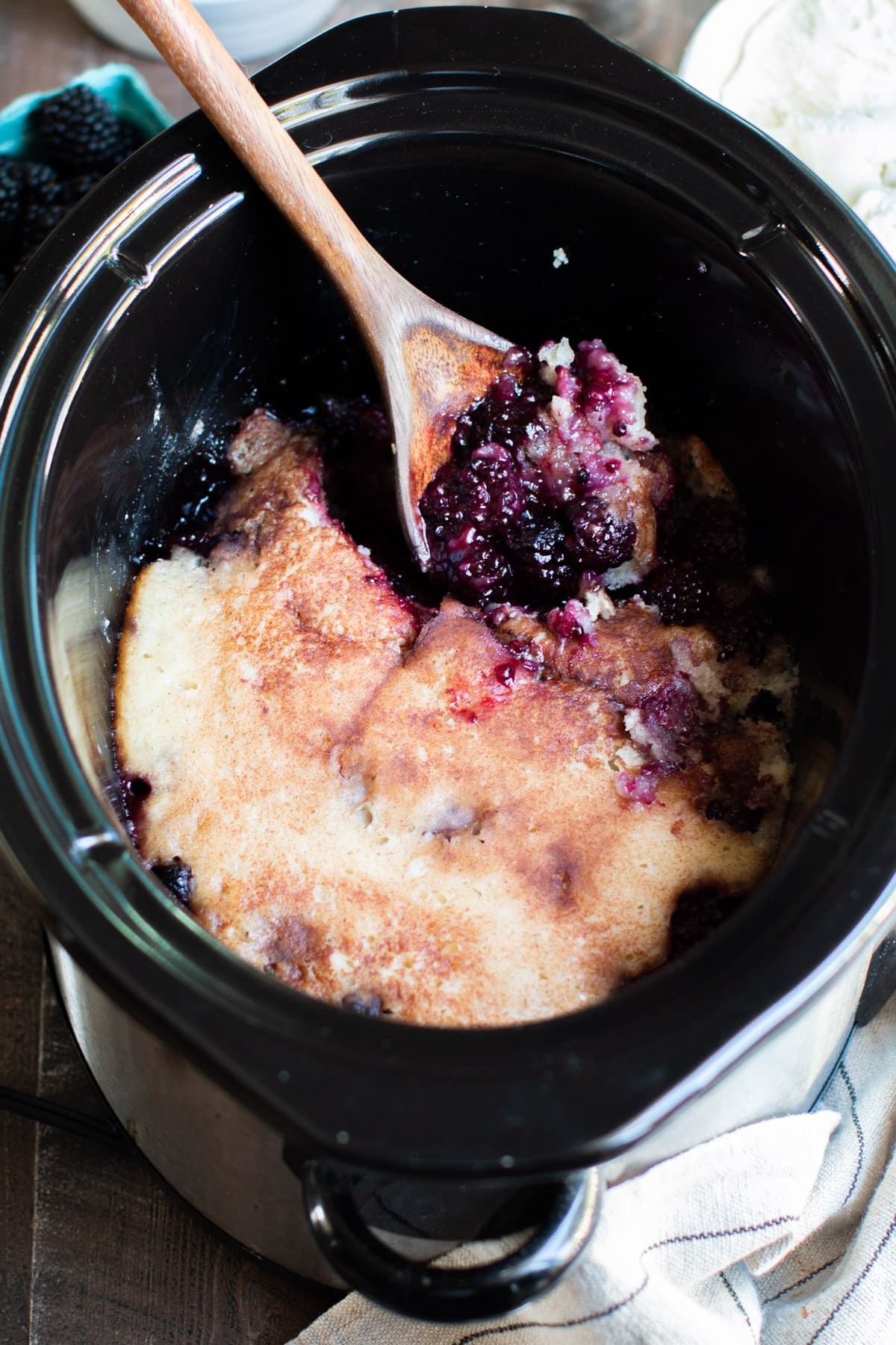 blackberry cobbler cooked in the slow cooker with spoon in it. Ice cream in the background.
