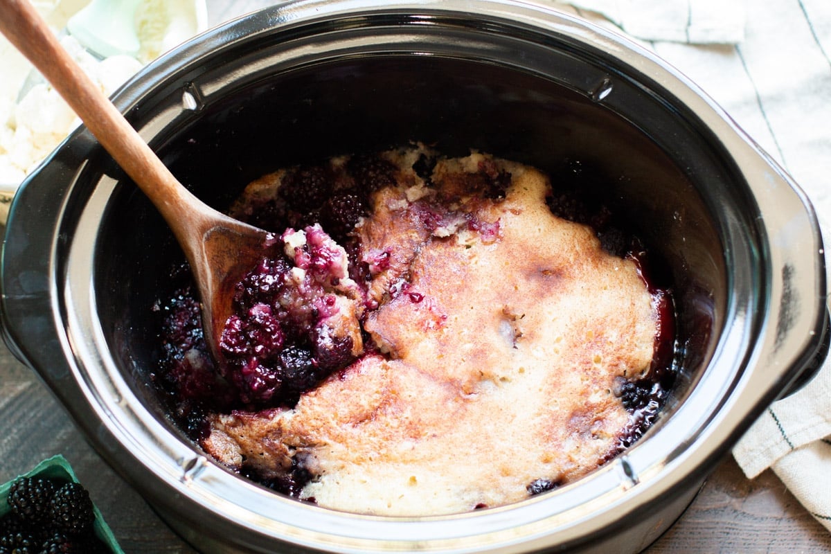 close up of blackberry cobbler in a slow cooker with spoonful of cobbler.