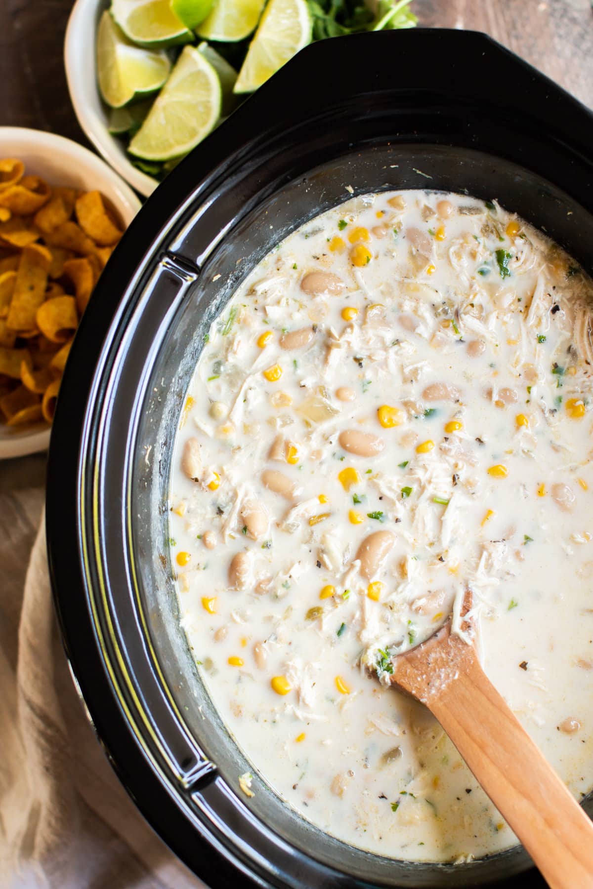 close up of white chicken chili in slow cooker with fritos in the background