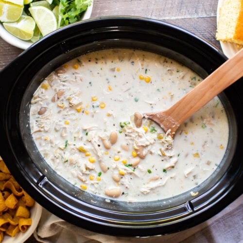 white chicken chili in slow cooker with wooden spoon in it.