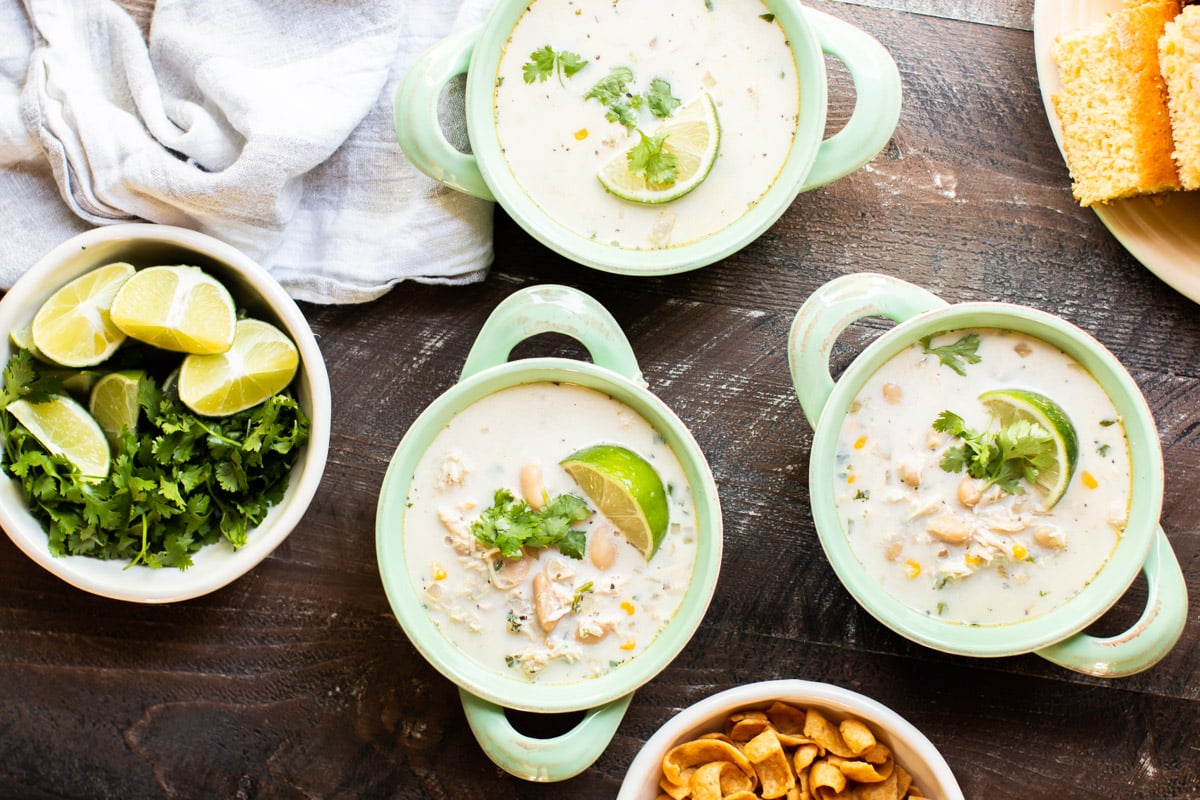 3 bowls of white chili with bowl of cilantro and limes on side