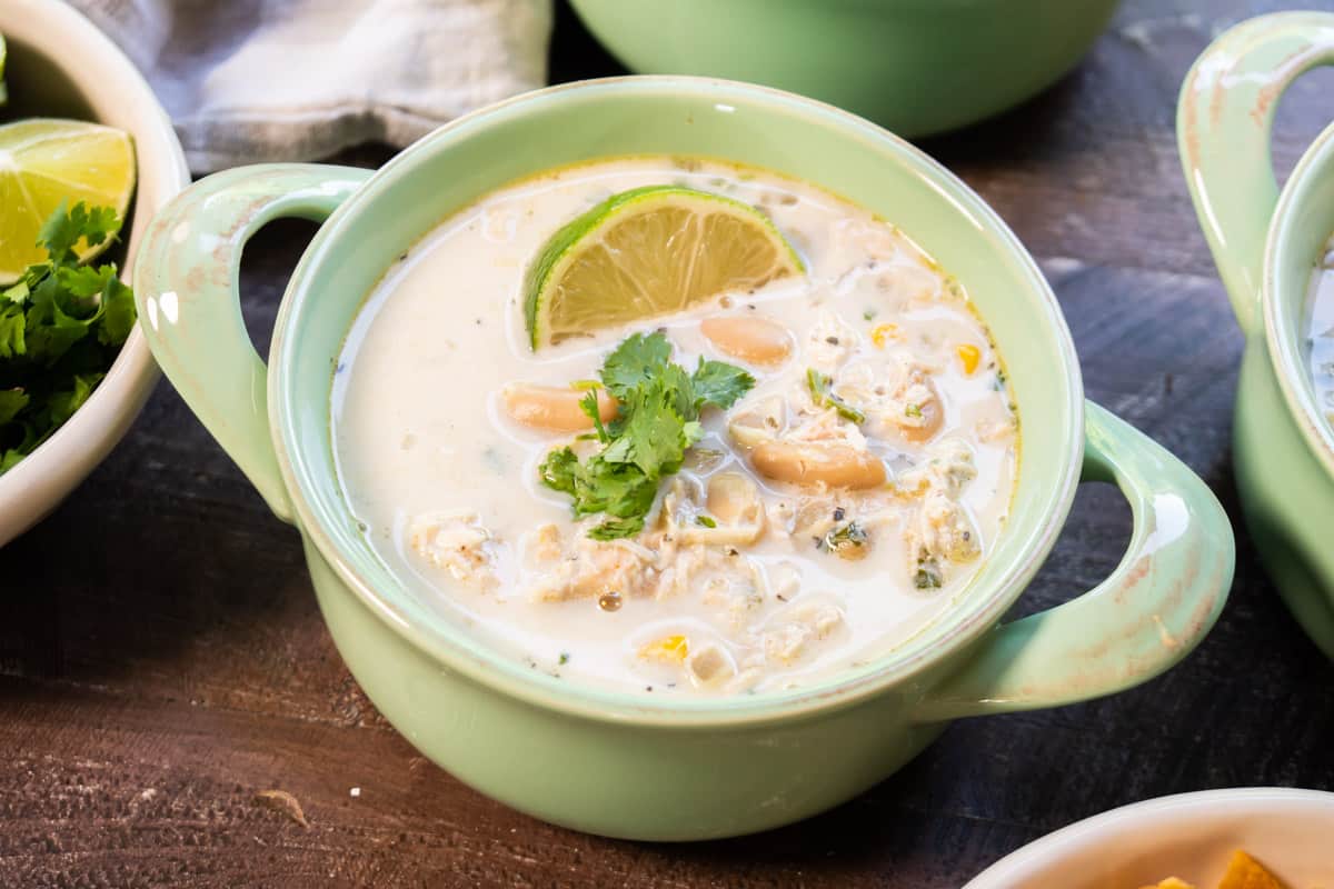 green bowl with white chicken chili in it. Lime and cilantro on top.