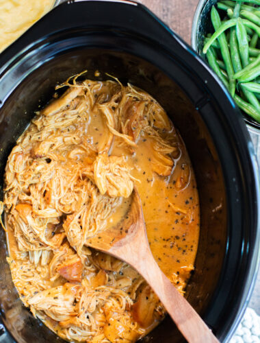 close up of shredded honey mustard chicken in slow cooker with green beans on the side.