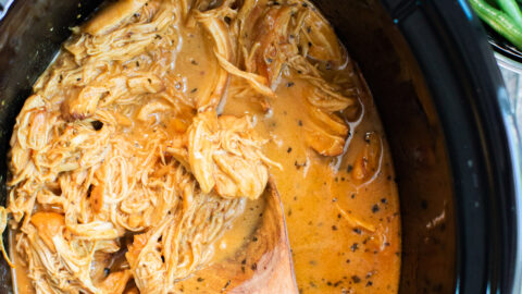 close up of shredded honey mustard chicken in slow cooker with green beans on the side.
